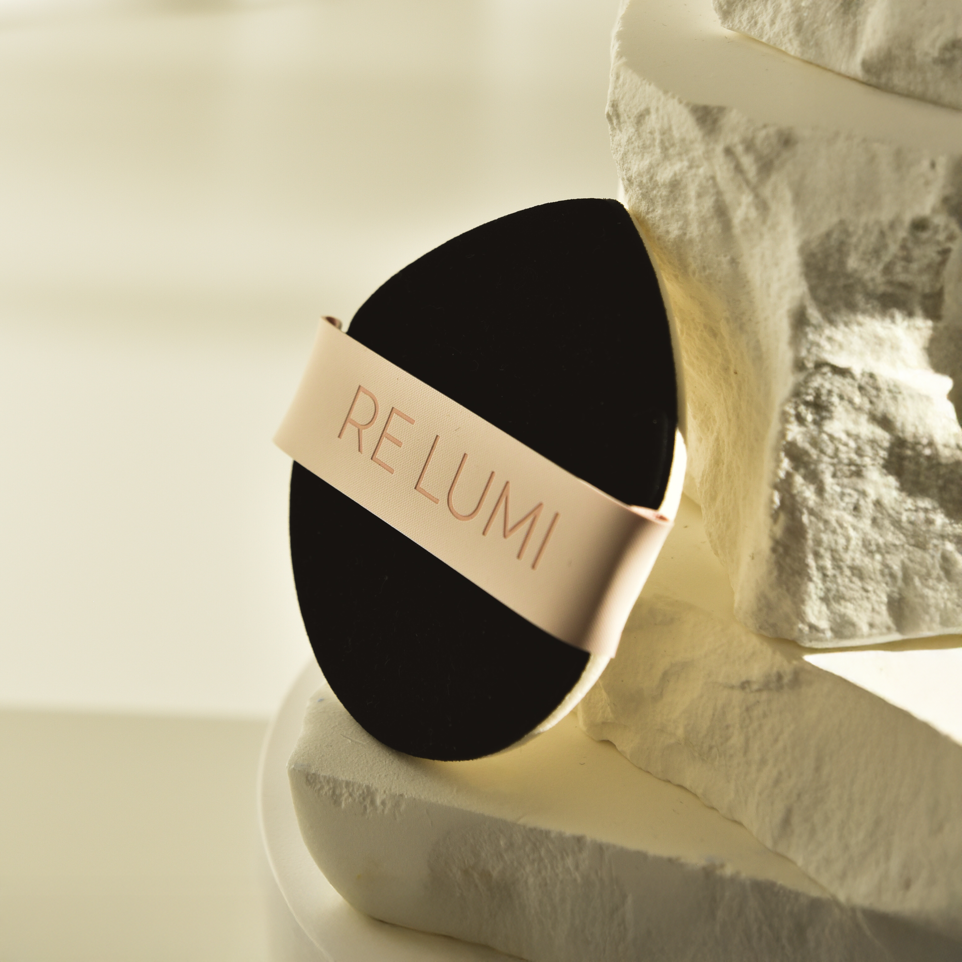 Black and beige RE LUMI bio based eco puff on a white surface with a blurred background