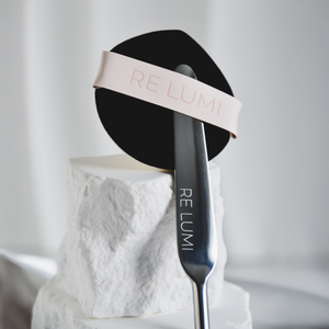 RE LUMI Spatula and Puff base signature duo on a white stone surface with a blurred background