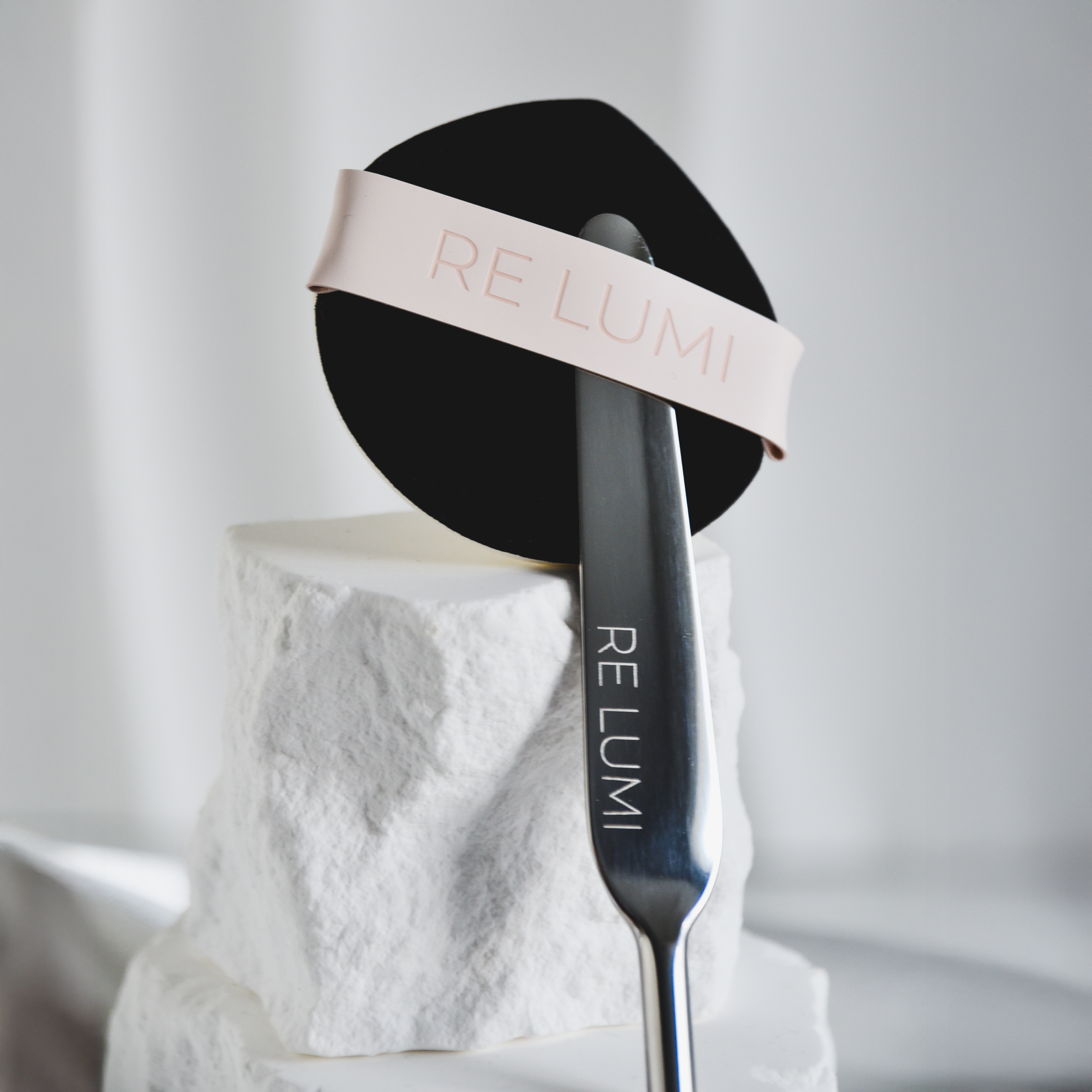 RE LUMI Spatula and Puff base signature duo on a white stone surface with a blurred background