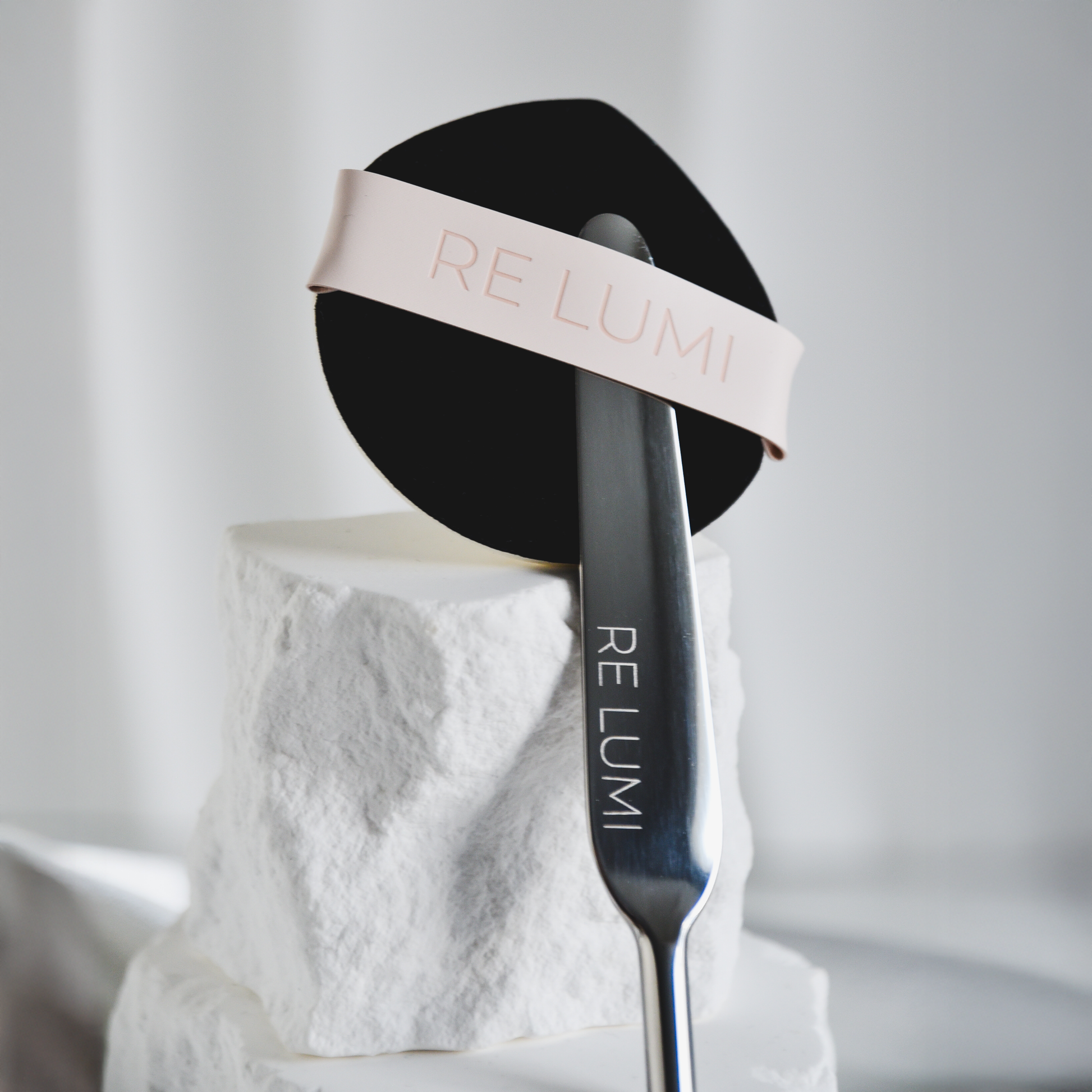 RE LUMI Spatula and Puff base signature duo on a white stone surface with a blurred background