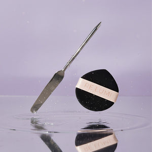 RE LUMI stainless steel spatula and black eco puff over water, highlighting purity, freshness, and sustainable K-beauty design.